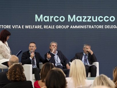 Evento corporate: panel di quattro relatori seduti su palco che discutono davanti al pubblico, grande schermo sullo sfondo con grafica testuale